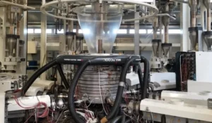 Industrial plastic extrusion and blow molding machine with multiple hoses and components, producing film or packaging material in a factory setting.