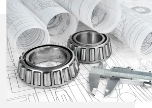 Two metal bearings, a caliper, and several engineering blueprints are arranged on a surface.