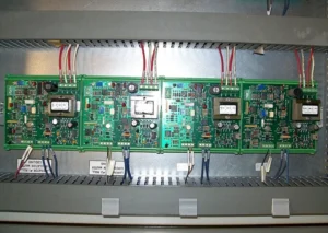 Four green circuit boards with various electronic components are mounted inside a slotted metal enclosure, connected by red and white wires.