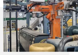 Industrial machinery and equipment arranged in a manufacturing setting, featuring a prominent orange robotic arm and various control units.