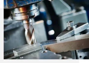 Close-up view of a metalworking drill bit machining a piece of metal in a workshop setting.