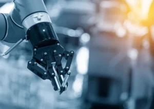 Close-up of a robotic arm with a gripper, positioned in an industrial environment with blurred machinery in the background.