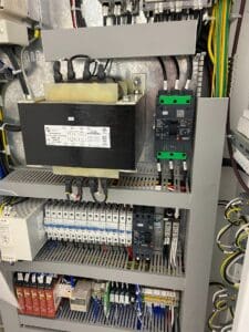 A view of an electrical panel with various circuits, wiring, and components, including a transformer and circuit breakers.